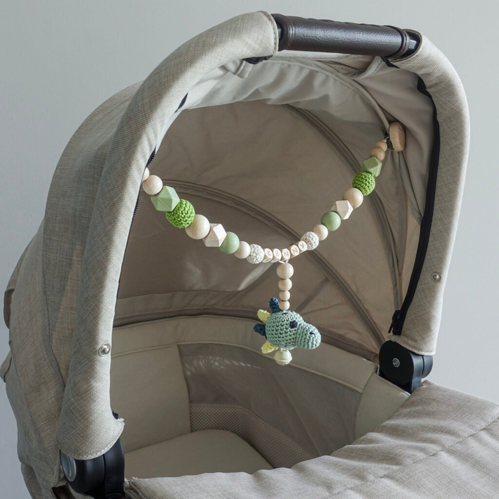 Personalisierte Kinderwagenkette mit gehäkeltem Dino am Kinderwagenverdeck befestigt